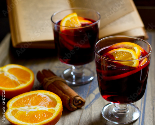 Mulled wine, book, orange and cinnamon on dark wooden background