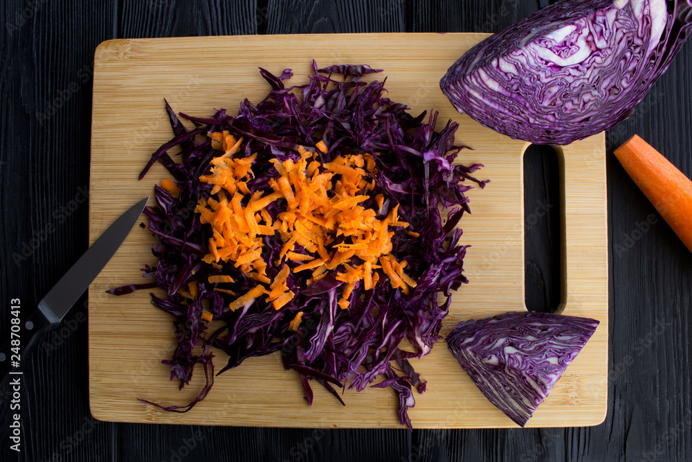 Chopped fresh blue cabbage and carrot on the brown  cutting board on the black wooden background.Top view.