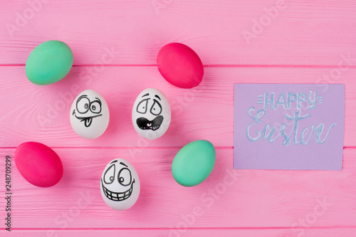 Various Easter eggs on pink background. Dyed Easter eggs and eggs with funny faces on colorful wooden background. Easter greeting card. photo