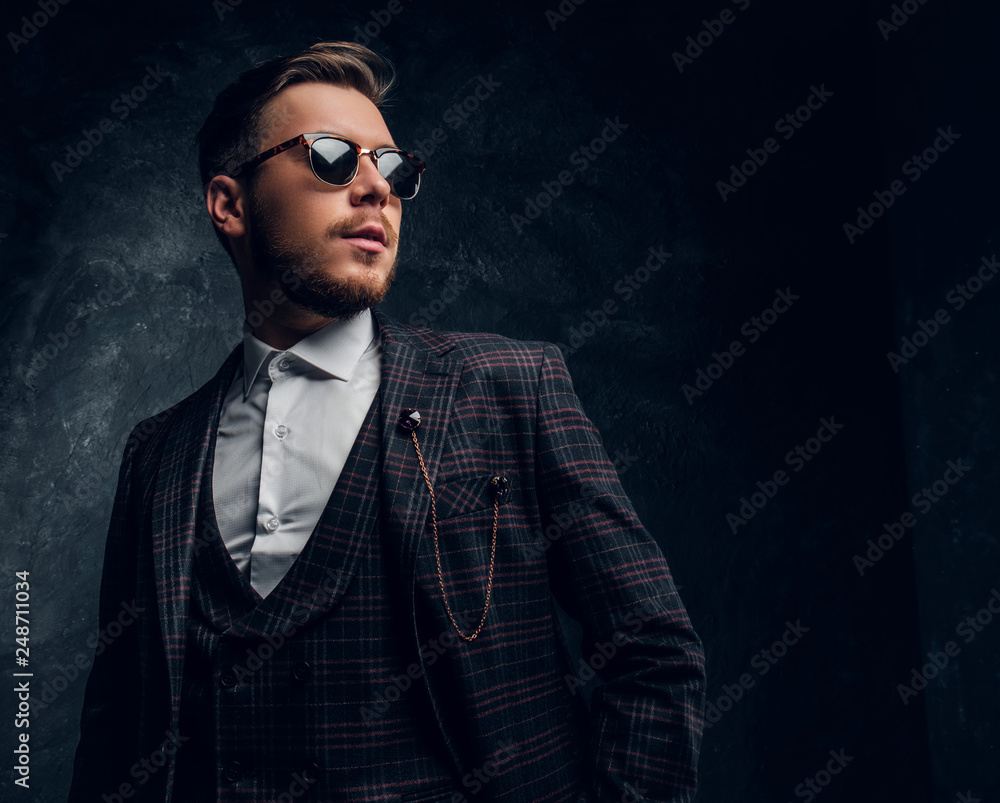 A confident elegantly dressed young man in sunglasses posing against a dark textured wall A confident elegantly dressed young man in sunglasses posing against a dark textured wall