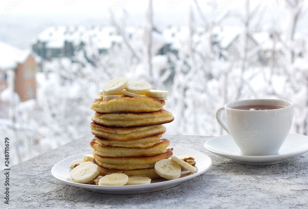 pancakes with honey, banana and nuts, a cup of tea, breakfast, view of the winter landscape pancakes with honey, banana and nuts, a cup of tea, breakfast, view of the winter landscape