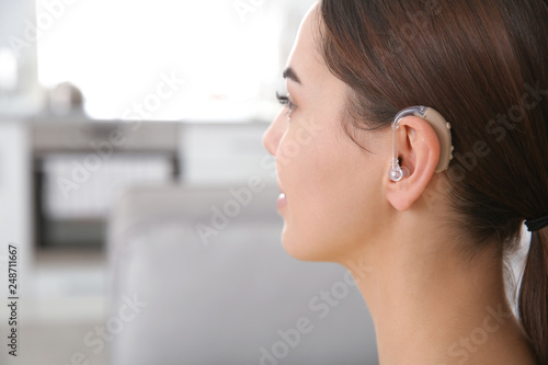 Young woman with hearing aid indoors, closeup. Space for text