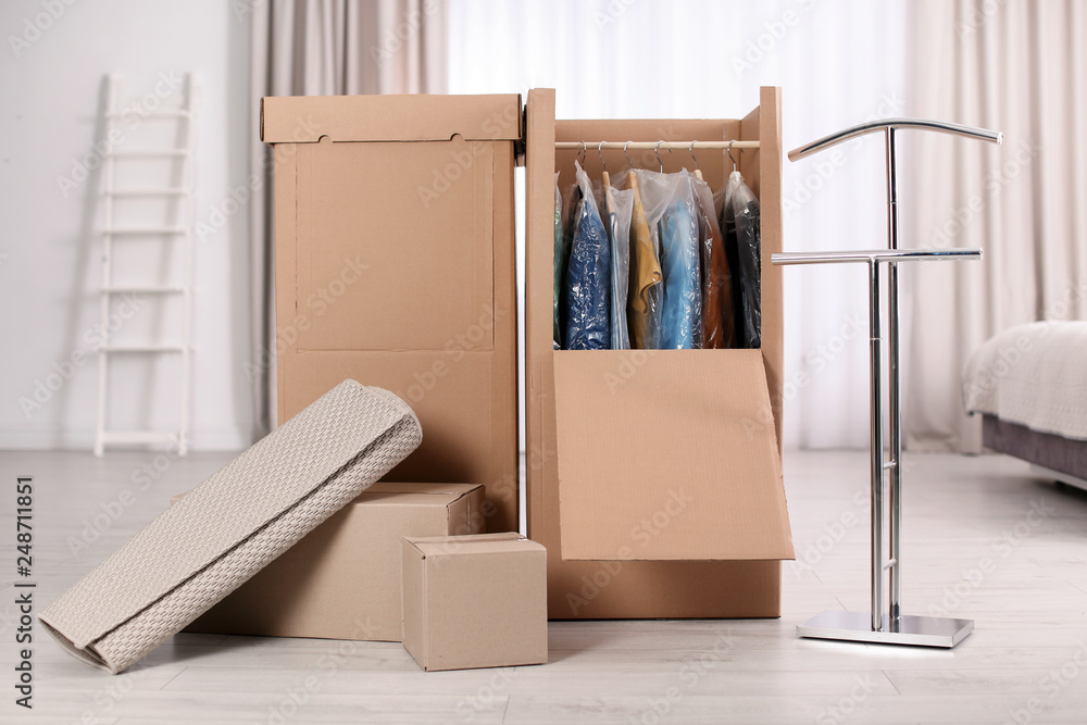 Fototapeta premium Cardboard wardrobe boxes with clothes on hangers and carpet indoors. Moving day