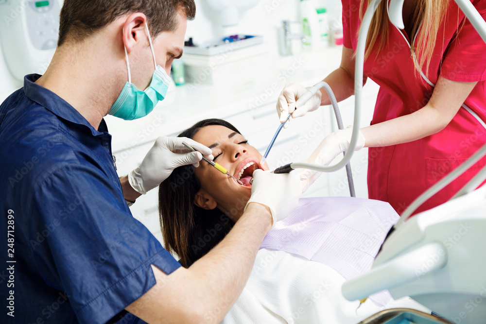 Fototapeta premium Concentrate dentist and his assistant drilling tooth to female patient on dental chair in dental clinic.