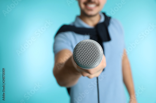 Young handsome man in casual clothes holding microphone on color background, closeup