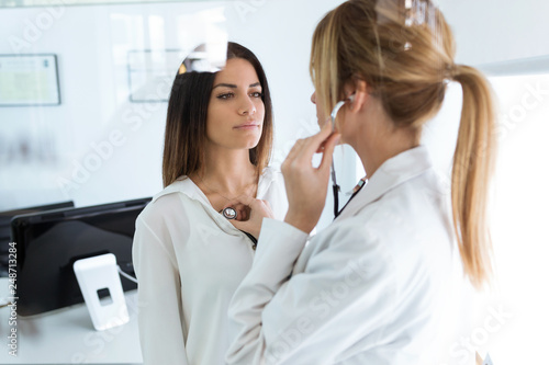 Confident woman being examined with stethoscope by doctor in the medical consultation.