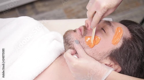 Concept of cosmetology and facial. A woman beautician makes face and beard modeling for a man waxing epilation