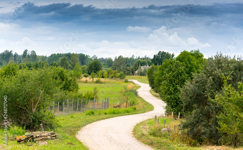 Ordinary rural landscape on a summer cloudy day. View from the hill on a winding country dirt road in summer. Prspective. © aleksandra_55