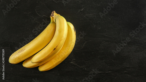 Top down view, bunch of yellow bananas on black board, space for text on right.