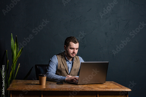 Young businessman working on his laptop on wooden table. Room for text. Dark background. Space for Text