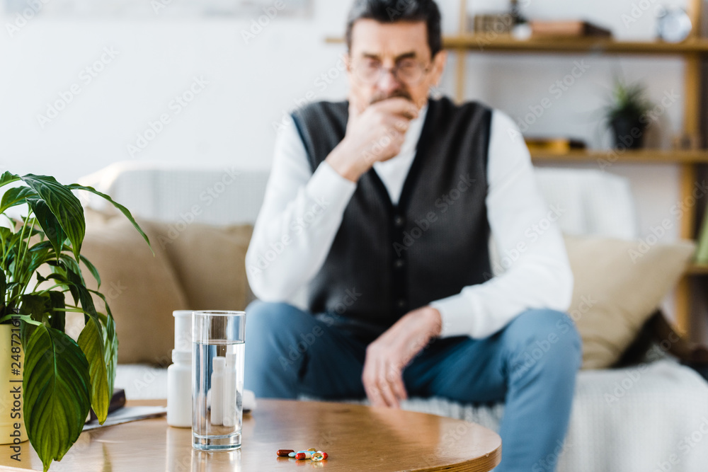selective focus of pills near glass of water with senior man on background selective focus of pills near glass of water with senior man on background