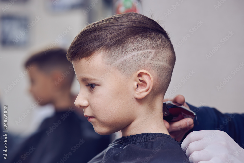 The portrait of a cute European boy in a barbershop. He is getting his new hairstyle.