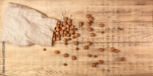 Large bag of burlap with walnuts and hazelnuts. Nuts are scattered on a large wooden board. Wooden background. Top view.