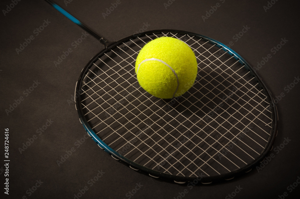 Green tennis ball and racket on dark