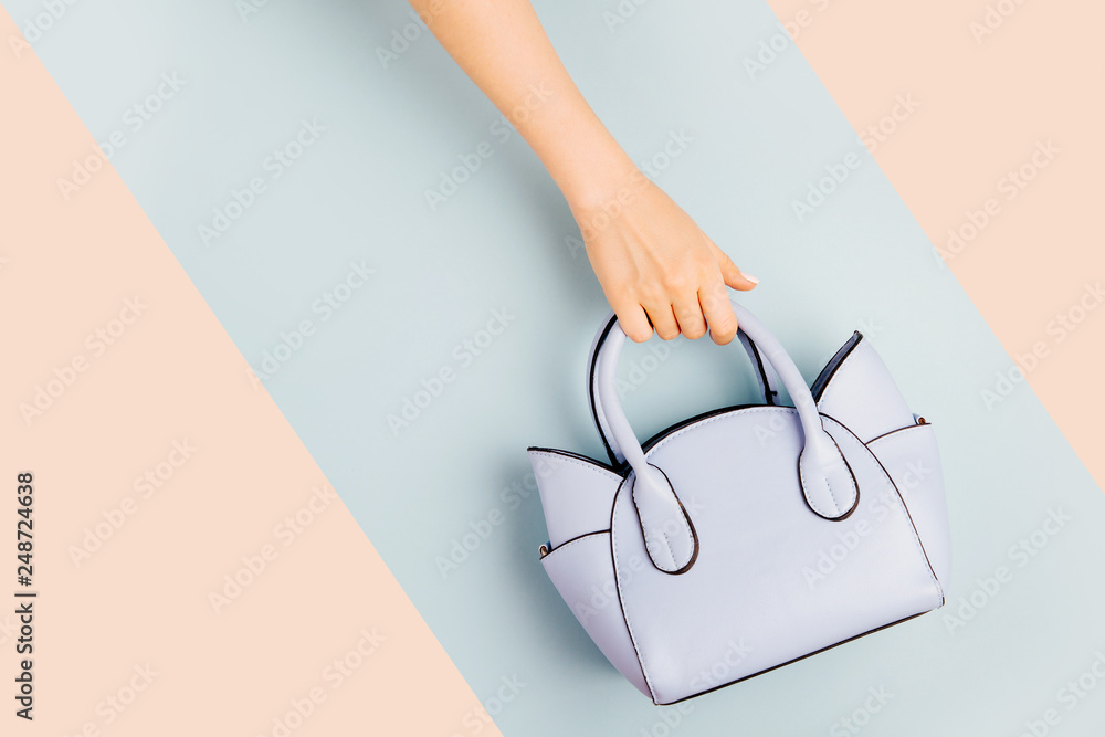 Female hands holds handbag on blue background . Flat lay, top view. Spring fashion concept in pastel colored