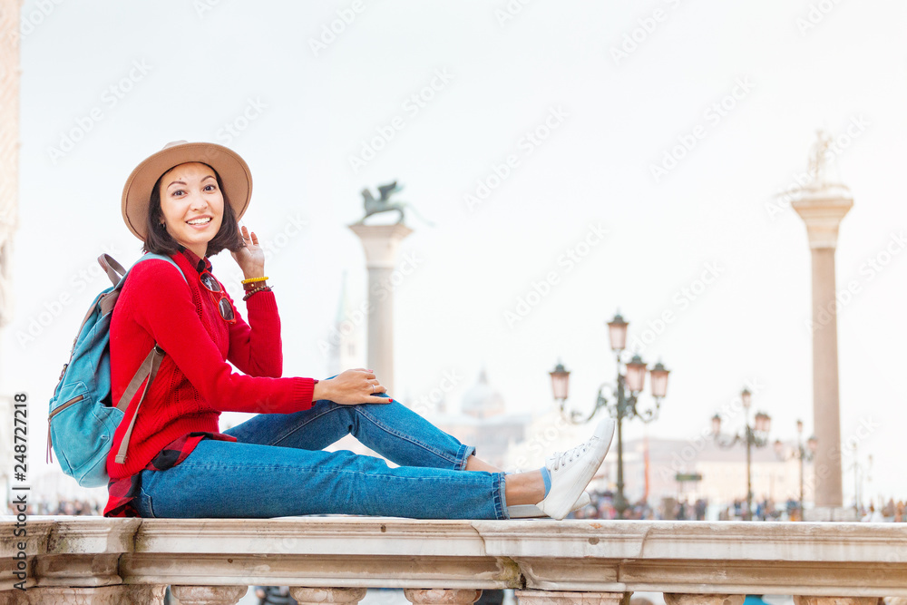 Φωτογραφία Young happy asian girl traveler with hat and backpack sitting on a parapet on San Marco square in Venice