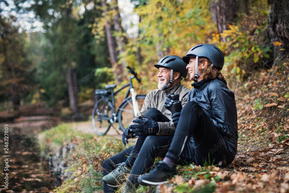 Fototapeta premium A senior couple with electrobikes sitting outdoors in park in autumn, resting.