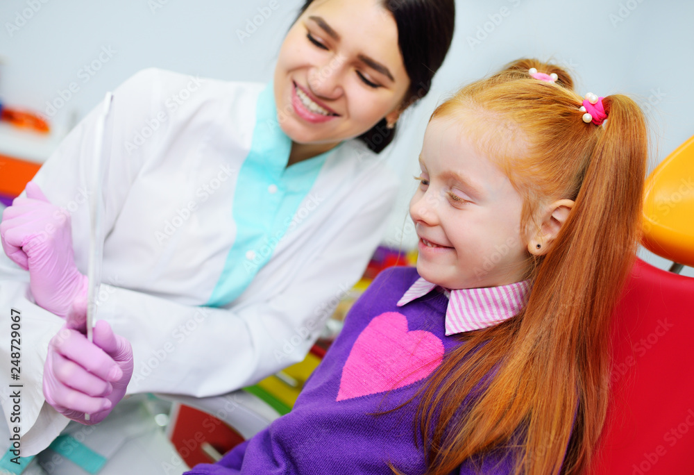 children's dentist examines the teeth and mouth of the child - a cute red-haired girl sitting in a dental chair children's dentist examines the teeth and mouth of the child - a cute red-haired girl sitting in a dental chair
