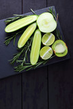 Green fruits, vegetables and rosemary on black background with copy space. Creative figure of natural green products. Cucumbers, kiwi, lime and green apple on slate board
