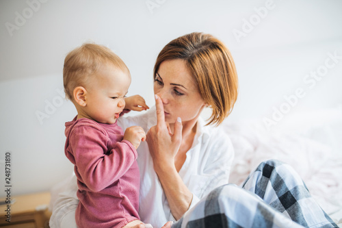 A young mother with little daughter sitting indoors on bed in the morning, playing.