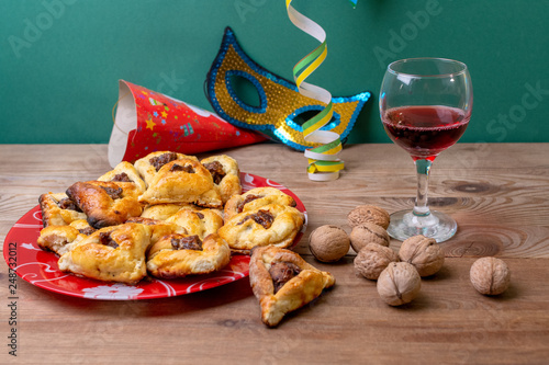 Carnival mask made of gold glitter, Multicolored festive triangular flags and Hamantaschen cookies on table. photo