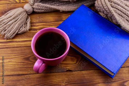 Cup of coffee, knitted scarf and book on wooden background