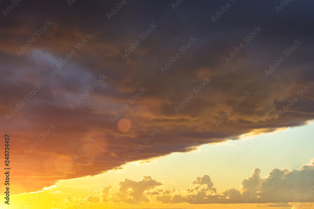 Dark sharp edge of a thundercloud front in front of a sunset sun, bright light.