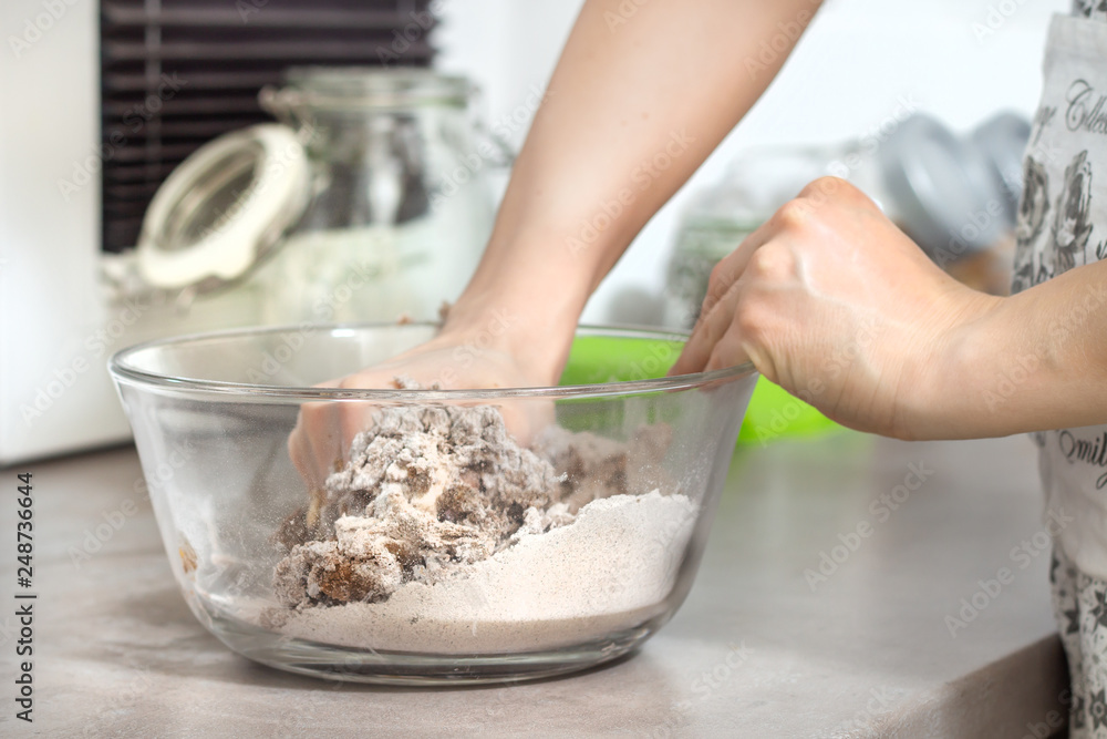 Dłonie kobiety wyrabiają ciasto na wypieki. Szklana miska ze składnikami stoi na kuchennym blacie. Dłonie kobiety wyrabiają ciasto na wypieki. Szklana miska ze składnikami stoi na kuchennym blacie.