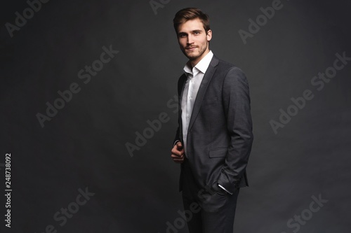 Portrait of a handsome young businessman dressed in suit isolated over gray background.