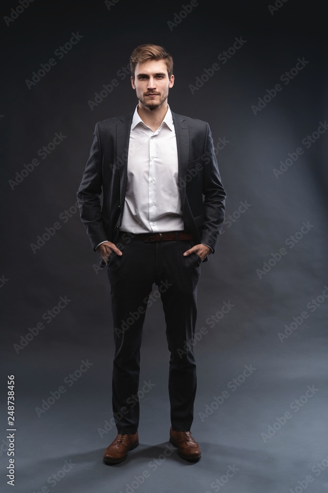 Full length portrait of a handsome young businessman dressed in suit isolated over gray background, posing, looking away, walking Full length portrait of a handsome young businessman dressed in suit isolated over gray background, posing, looking away, walking