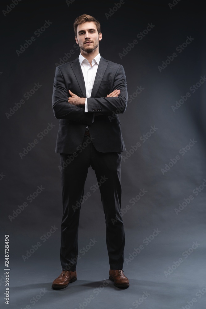 Full length portrait of a handsome young businessman dressed in suit isolated over gray background, posing, looking away, walking Full length portrait of a handsome young businessman dressed in suit isolated over gray background, posing, looking away, walking