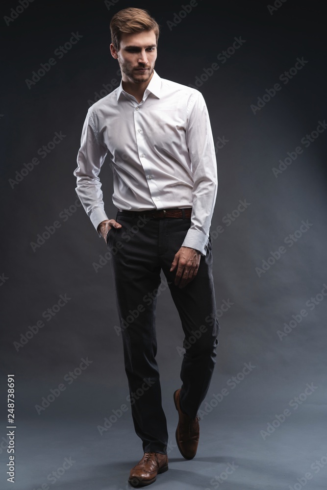 Full length portrait of a handsome young businessman dressed in suit isolated over gray background, posing, looking away, walking Full length portrait of a handsome young businessman dressed in suit isolated over gray background, posing, looking away, walking