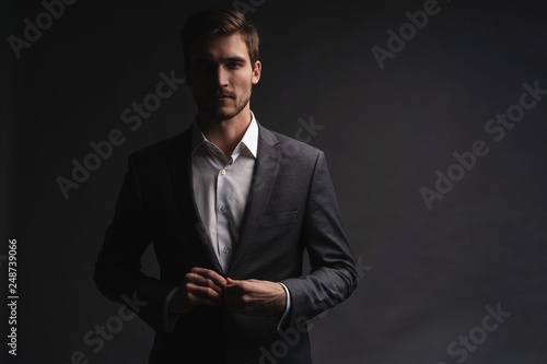 Portrait of serious handsome man in gray suit buttoning jacket