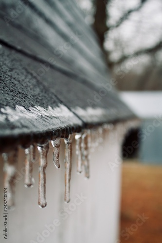 A frigid day full of icicles hanging off the roof of a small shed in front of the barn.