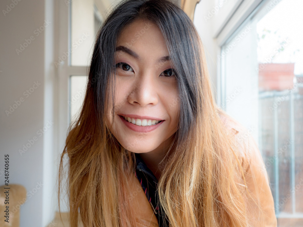 A portrait of excited Asian young woman sitting at home and looking at camera with joy, happy face. Adorable lady glad to see friend, family making video call by Internet. A portrait of excited Asian young woman sitting at home and looking at camera with joy, happy face. Adorable lady glad to see friend, family making video call by Internet.