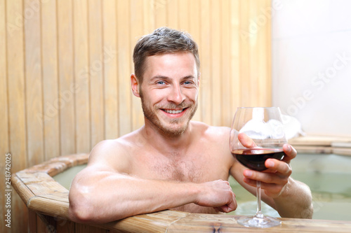 Kąpiel w winie, mężczyzna relaksuje się w spa z kieliszkiem czerwonego wina.