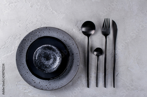 Set of porcelain handcraft  grey and black plates and  bowls cutlery set, linen napkin on a white wooden table. Flat lay