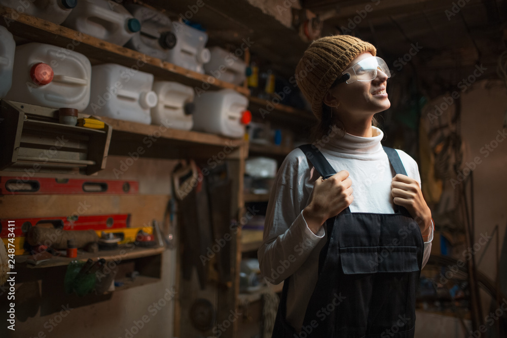 Portrait of smiling young builder girl standing in old workshop room, wearing construction glasses. Portrait of smiling young builder girl standing in old workshop room, wearing construction glasses.