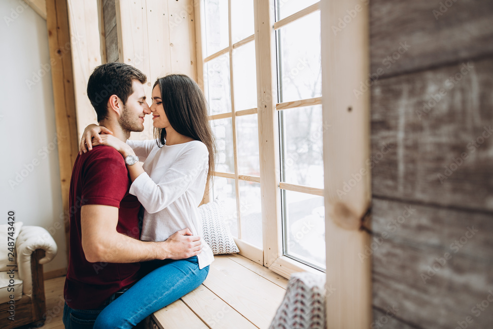 Couple in love. Happy couple hugging near the window. The guy hug his beautiful girl. They are happy spending time together Couple in love. Happy couple hugging near the window. The guy hug his beautiful girl. They are happy spending time together