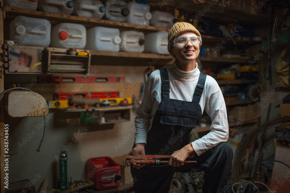 Portrait of smiling young builder girl standing in old workshop room, wearing construction glasses. Portrait of smiling young builder girl standing in old workshop room, wearing construction glasses.