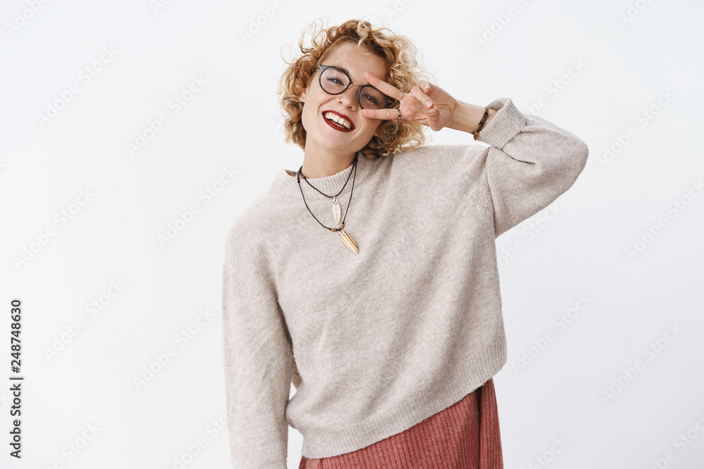 Enthusiastic happy and sincere carefree lgbt woman in glasses and stylish sweater showing peace or victory gesture near eye and smiling broadly having fun over white background spread happiness
