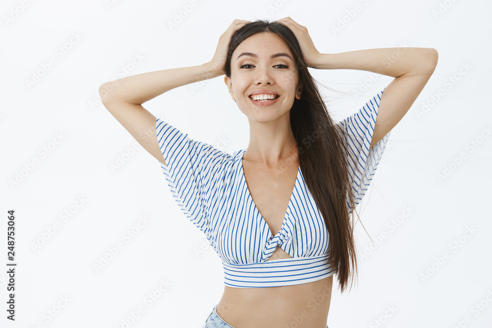 Waist-up shot of feminine and sensual attractive confident woman in cropped blouse holding hands on head carefree and satisfied with ocean breeze smiling broadly at camera enjoying vacation Waist-up shot of feminine and sensual attractive confident woman in cropped blouse holding hands on head carefree and satisfied with ocean breeze smiling broadly at camera enjoying vacation