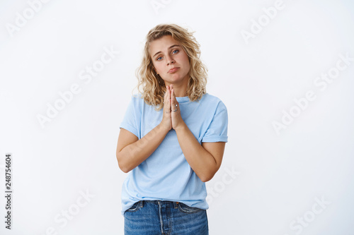 Please I beg you. Portrait of cute whining blonde woman asking favour being in need making sorrow face pursing lips and holding hands in pray as asking help, supplicating over white background