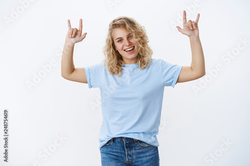 Rock this party up. Portrait of excited and cool good-looking blonde young woman having fun dancing and enjoying atmostphere at concert raising hands with rock-n-roll gesture smiling pleased photo