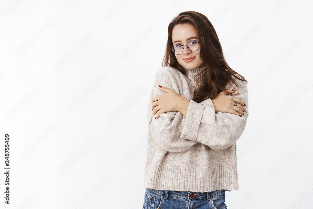 Soft and tender happy young sensual woman in glasses and sweater hugging herself as warming up in cozy outfit, smiling at camera cute and silly waiting boyfriend bring cacao over gray background Soft and tender happy young sensual woman in glasses and sweater hugging herself as warming up in cozy outfit, smiling at camera cute and silly waiting boyfriend bring cacao over gray background