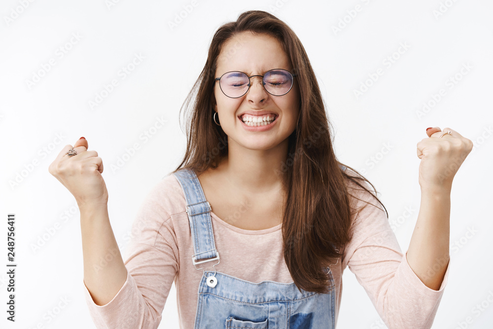 Obraz premium Happy relieaved woman triumphing as finally gaining goal or success clenching teeth delighted raising clenched fists in victory and celebration being glad fulfill dream over gray background