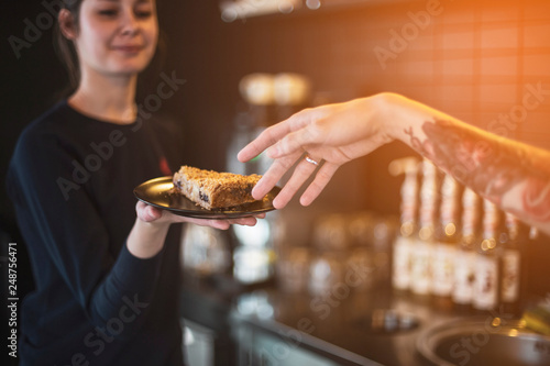 waiters are fun at work  the hand of a boy who stretches to a plate with a cake kept by a smiling girl waiter in a cafe.