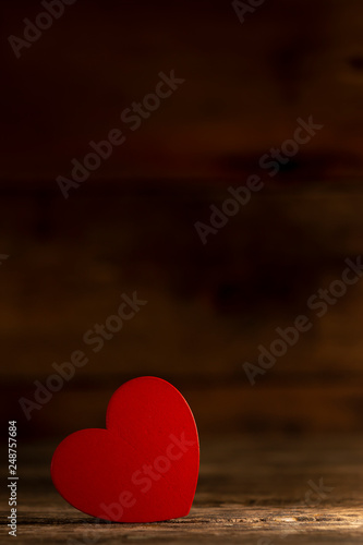 Closeup of bright red heart-shaped decorative element in ray of sunlight on wooden table 