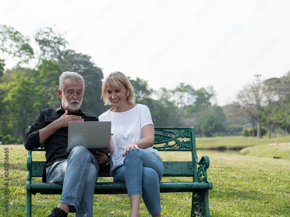 Senior man and woman couple connected on laptop computer in a park on a sunny day. relax in the forest spring summer time. free time, lifestyle retirement grandparents concept. Senior man and woman couple connected on laptop computer in a park on a sunny day. relax in the forest spring summer time. free time, lifestyle retirement grandparents concept.