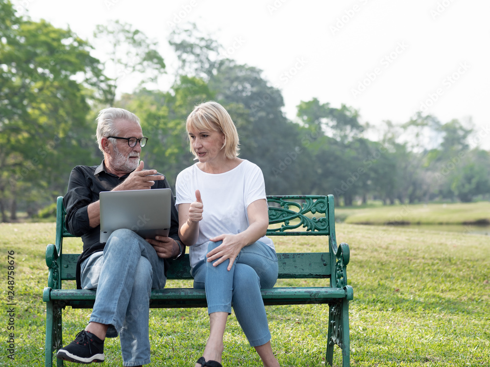 Senior man and woman couple connected on laptop computer in a park on a sunny day. relax in the forest spring summer time. free time, lifestyle retirement grandparents concept. Senior man and woman couple connected on laptop computer in a park on a sunny day. relax in the forest spring summer time. free time, lifestyle retirement grandparents concept.